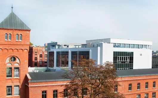 Instytut Fizyki: pofabryczny budynek z czerwonej cegły z wieżyczką. W tle biały nowoczesny budynek