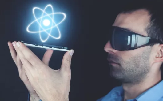 Mężczyzna w ciemnych okularach trzymający smartfona, nad którym widnieje ikona atomu
