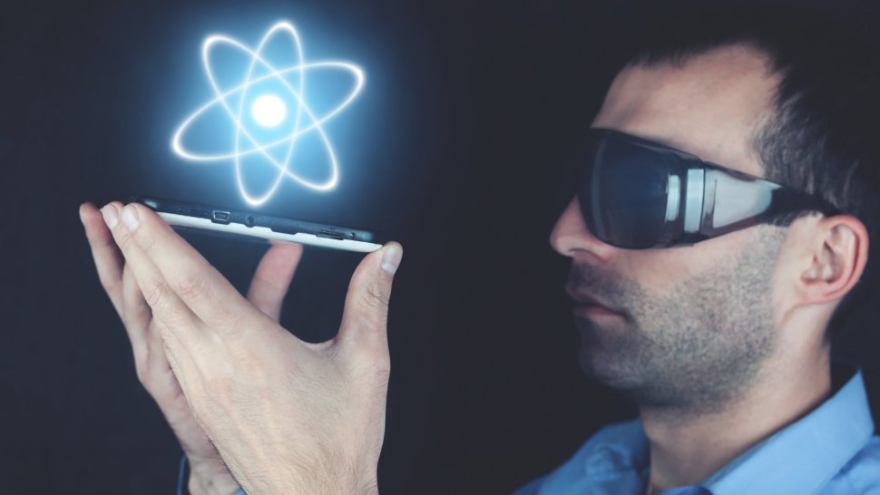 Mężczyzna w ciemnych okularach trzymający smartfona, nad którym widnieje ikona atomu