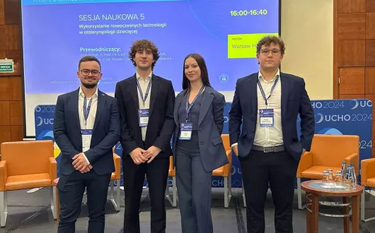 Elegancko ubrani - autorzy aplikacji stojący na podeście, na tle wyświetlanej planszy konferencyjnej.
