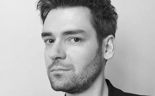 Czarno-biały portret dra. inż. Krzysztofa Guzka na tle jasnej ściany z widocznym fragmentem czarnej, eleganckiej odzieży.