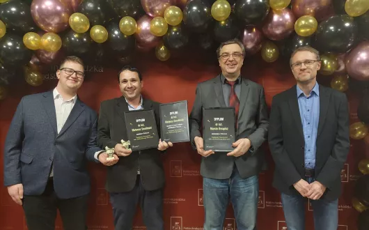Przewodniczący WRS FTIMS Jakub Samek, dr inż. Mateusz Smoliński z nagrodami, dr inż. Marcin Kwapisz z nominacją i Prodziekan Marek Galewski w eleganckich ubraniach na tle ścianki politechnicznej z balonami.