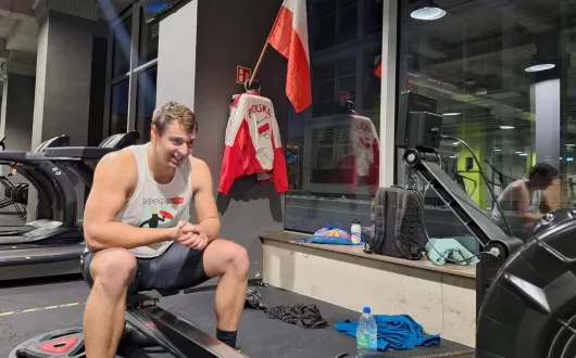 Tomasz Józefiak podczas zawodów, na siłowni. W tle bluza polskiej reprezentacji i flaga Polski.