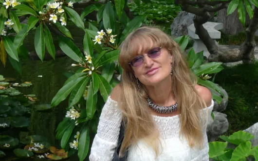 Zdjęcie portretowe: prof. Urszula Ledzewicz w białej bluzce na tle zieleni.