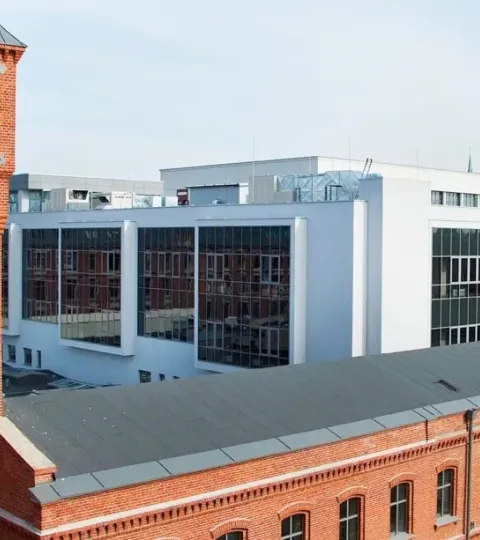 Instytut Fizyki: pofabryczny budynek z czerwonej cegły z wieżyczką. W tle biały nowoczesny budynek