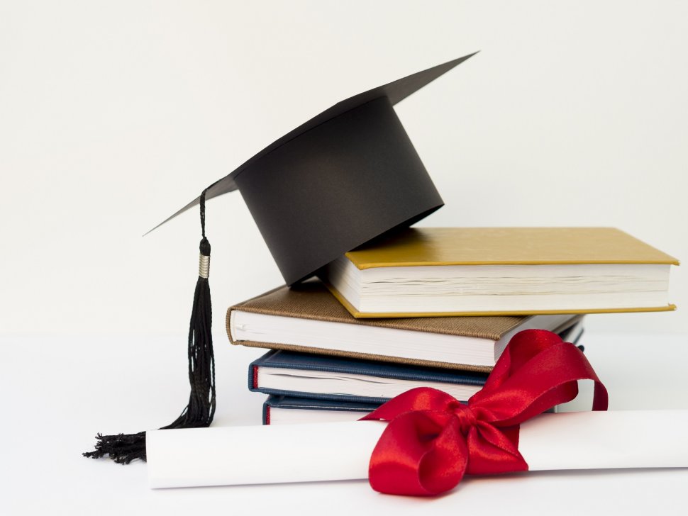 czapka akademicka na stosie książek i dyplom związany czerwoną wstążką