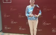 Nagrodzona prof. Aneta Poniszewska-Marańda trzyma statuetkę na tle bordowej ścianki Politechniki Łódzkiej. 