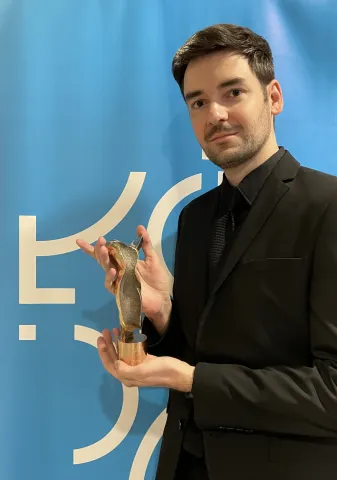 Dr Guzek prezentujący złota statuetke na tle niebieskim tle