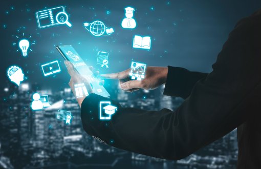 Człowiek trzymający smartfon. Na ekranie napis E-learning. Wokół ikony portalu dydaktycznego.