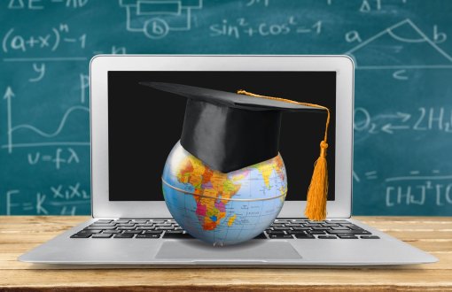 Globus z czapką akademicką na tle otwartego laptopa. Na dalszym planie tablica z zapisanymi kredą wzorami.