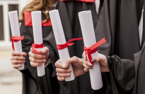 Czworo absolwentów trzyma dyplomy owinięte czerwoną wstążką