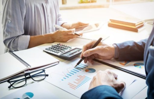 Pracownicy administracji opracowują dane finansowe. Na stole kalkulator, okulary i dokumenty z wykresami